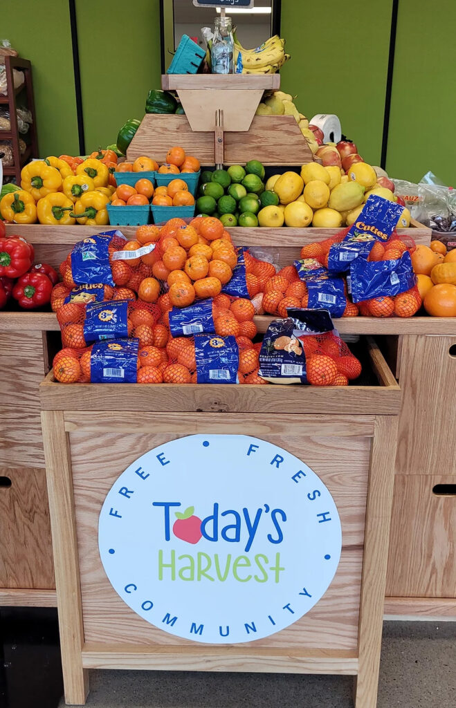 There is a 3-tiered table filled with produce such as oranges and peppers—a Today's Harvest logo on the front.